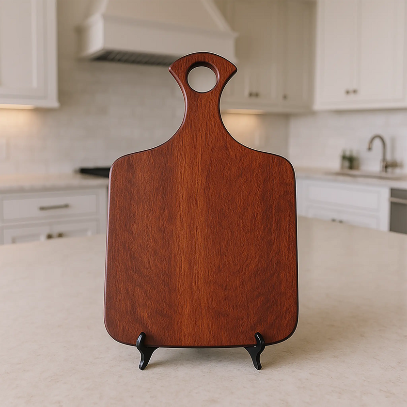 Bloodwood charcuterie board with rounded handle standing on tabletop in modern kitchen.