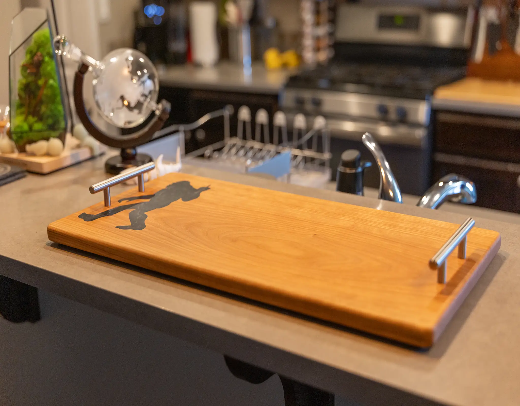 Angled shot of cherry wood charcuterie board featuring brushed aluminum handles, displayed on a modern kitchen island.