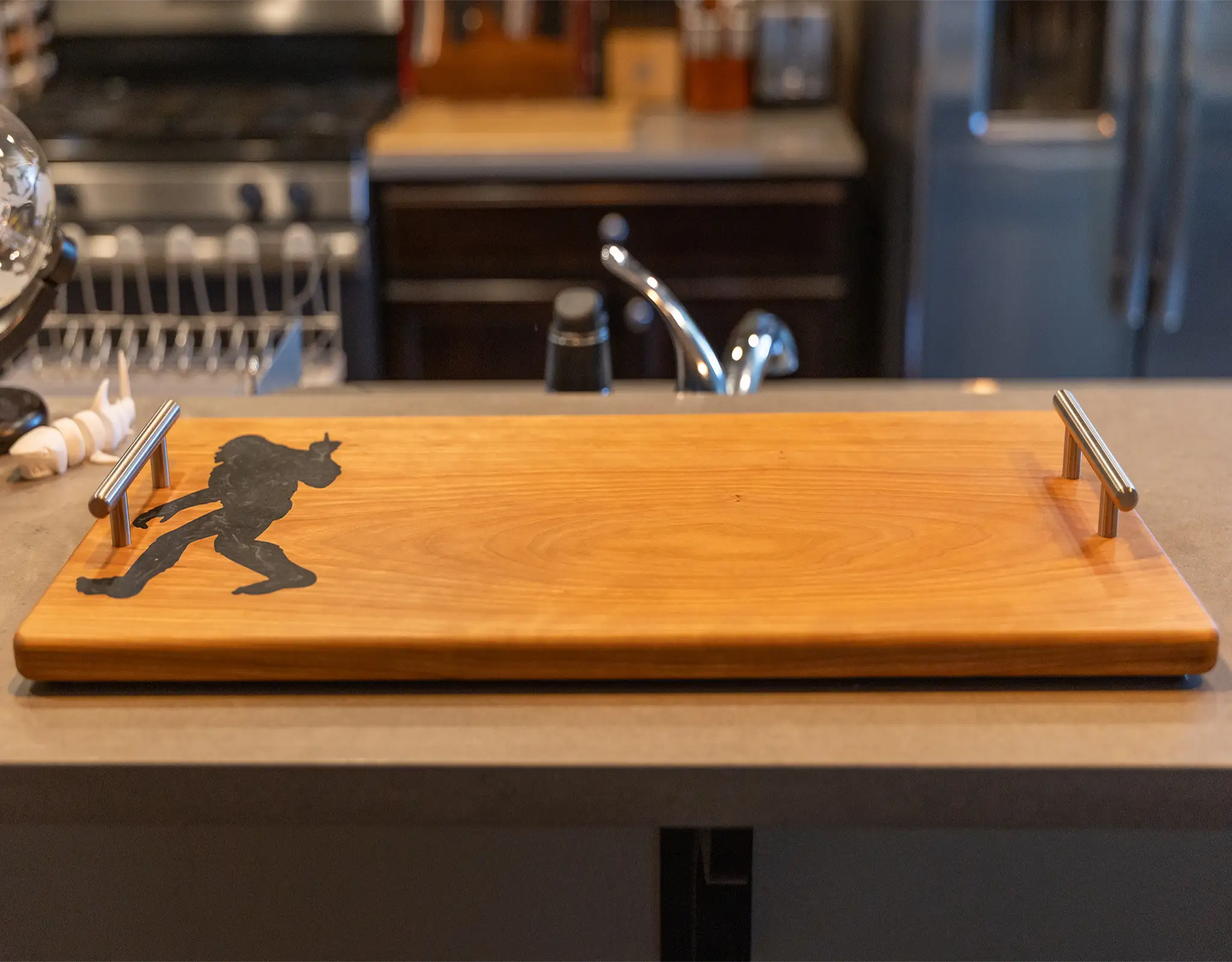 Cherry wood charcuterie board with brushed aluminum handles, straight-on view on a light kitchen countertop.