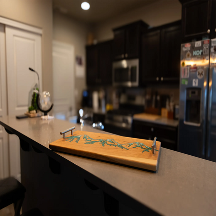 Handcrafted cherry wood charcuterie board featuring a green epoxy mountain inlay displayed on a kitchen countertop.