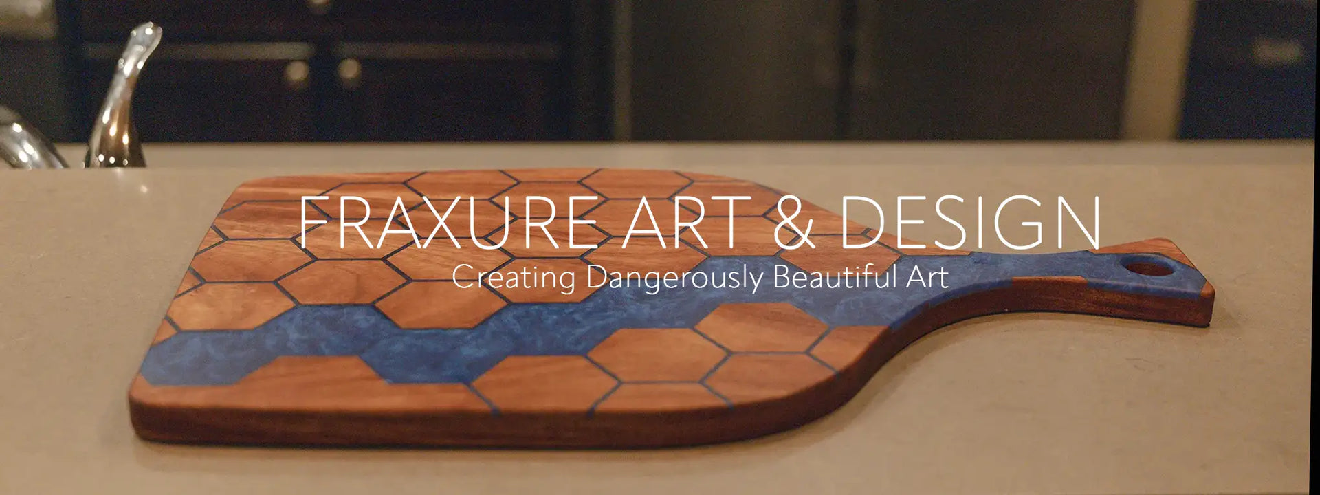 Hexagon inlay wood charcuterie board with blue epoxy river on kitchen counter – Fraxure Art & Design hero image.