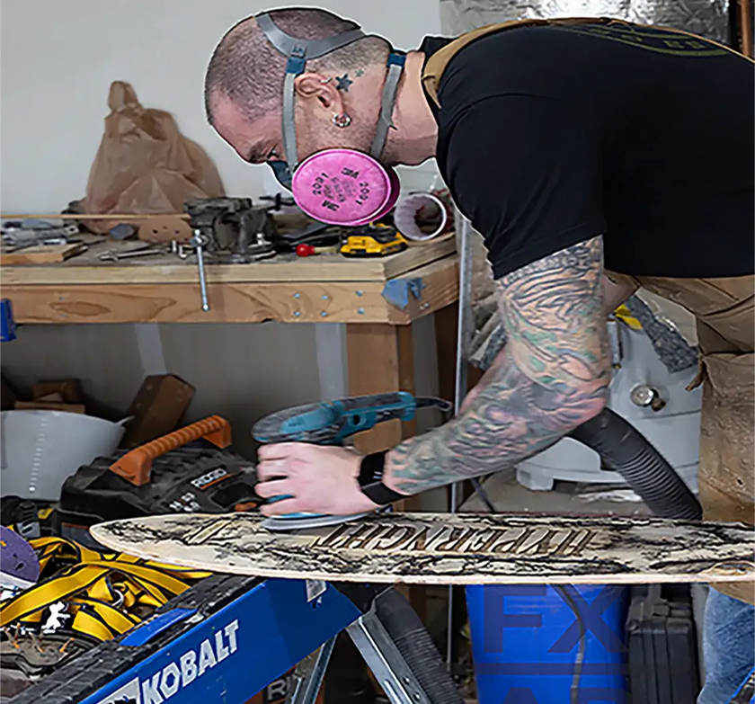 Craftsman sanding a handcrafted longboard at Fraxure Art & Design, highlighting precision woodworking and artistry.